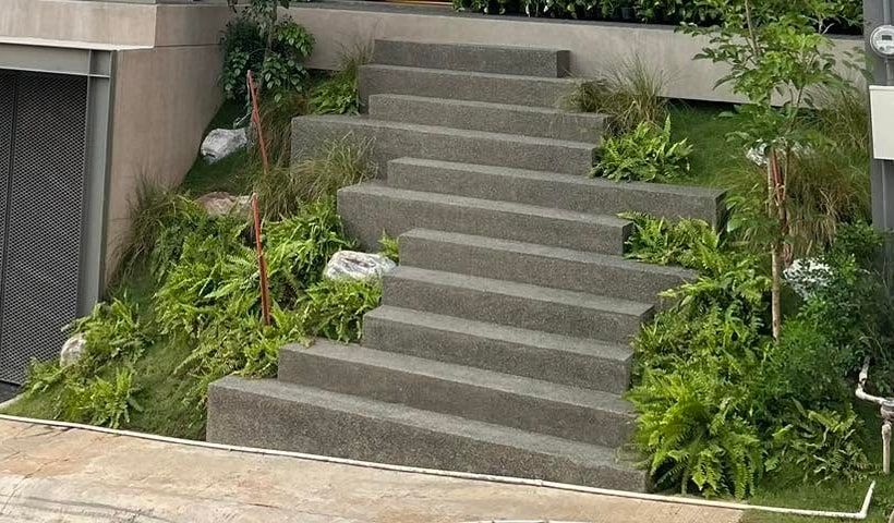 Ferns, grasses, and pale boulders planted on the slope beside wide concrete stairs